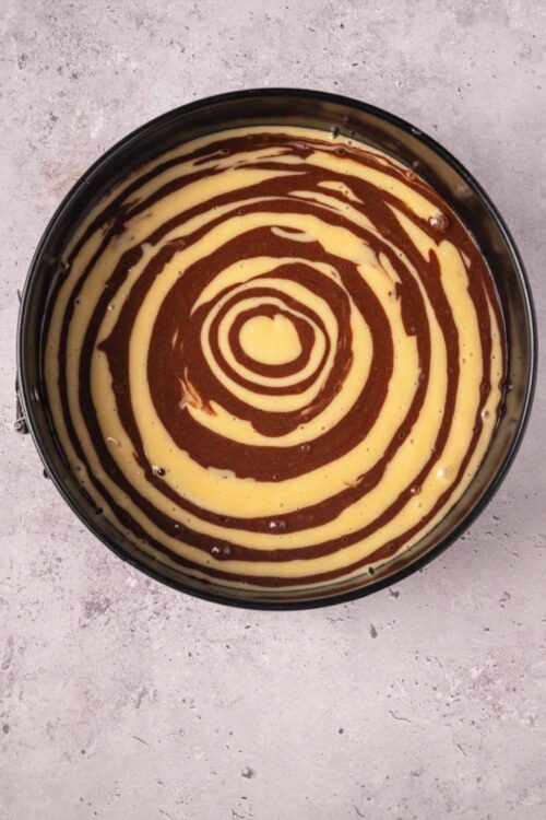 Swirled vanilla and chocolate cheesecake batter in a round cake pan.
