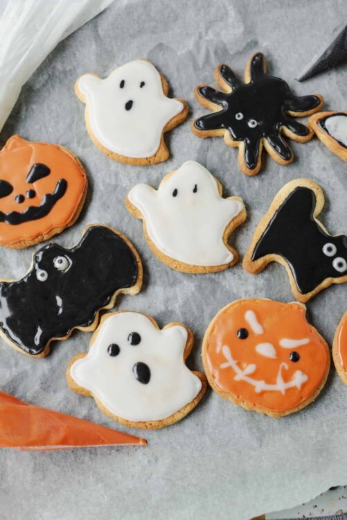 Spooky Halloween ghost, pumpkin, and bat decorated sugar cookies on parchment paper.