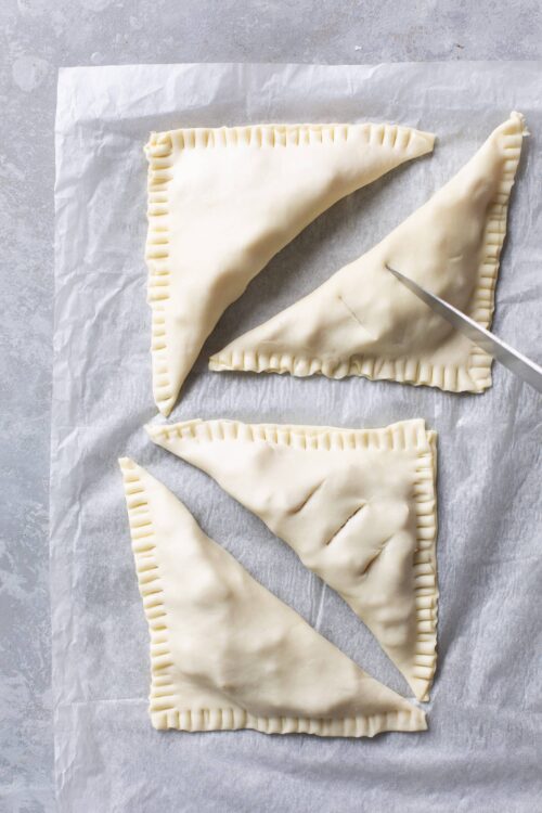 Buttered homemade hand pies on parchment paper, ready for baking.