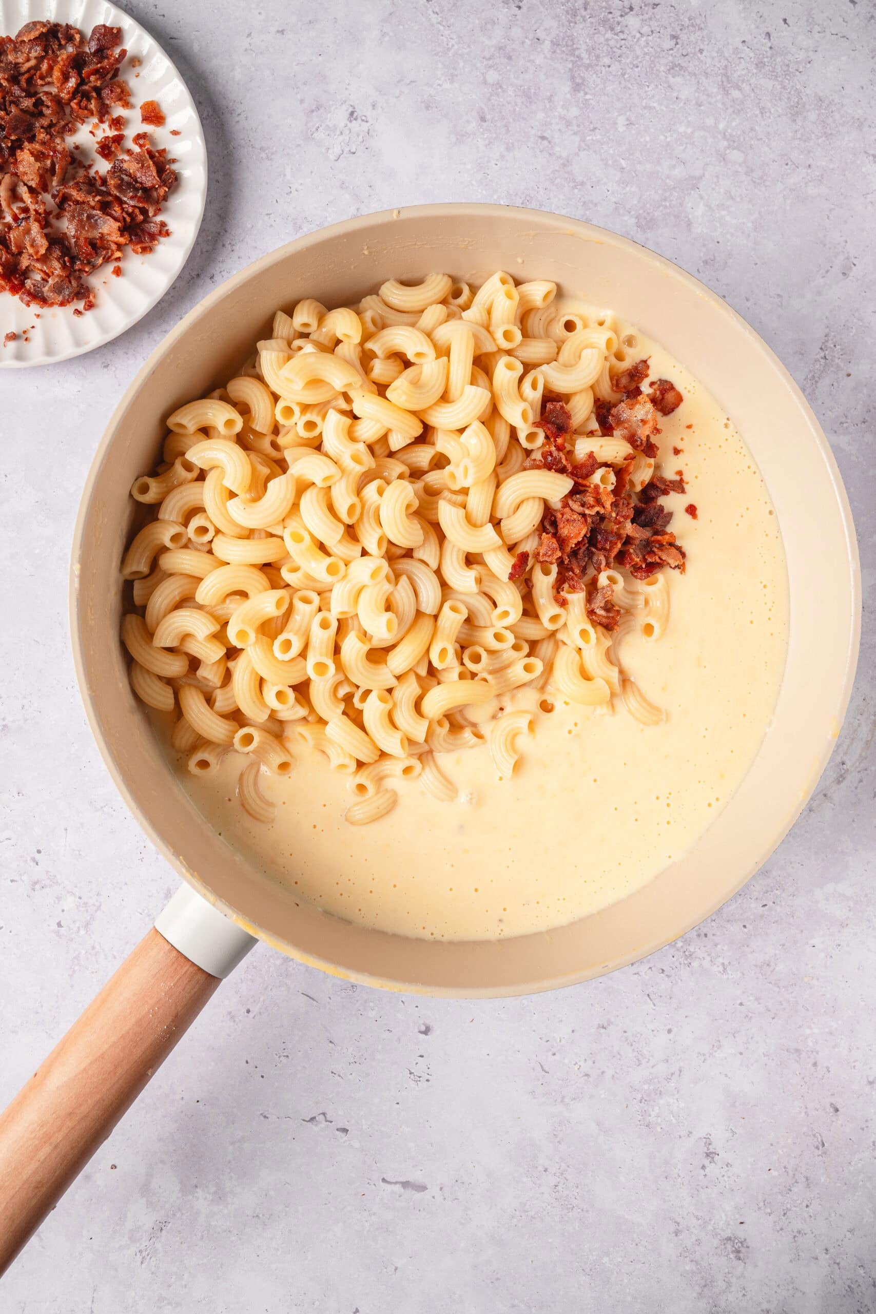 Creamy macaroni and cheese with crispy bacon bits in a beige skillet.