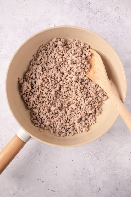 Ground turkey in a beige skillet for baking recipes, with a wooden spatula on the side.
