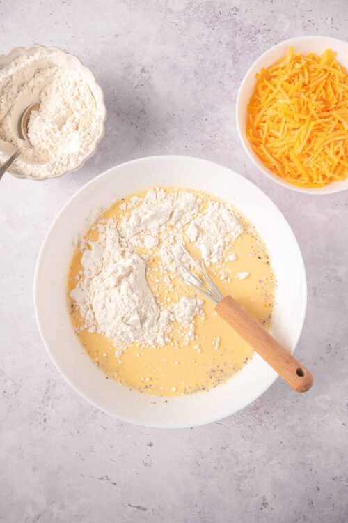 Flour, eggs, shredded cheddar cheese, and baking ingredients for homemade cheesy bread.