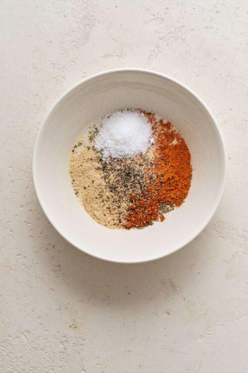 Ground spices in white bowl for baking or cooking, close-up, on light textured background.