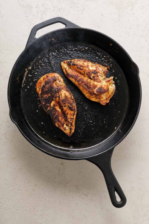 Buttermilk chicken breasts frying in a cast iron skillet with crispy, golden-brown crust.