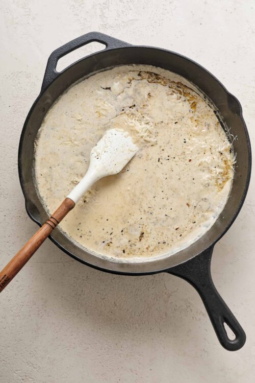 Creamy garlic parmesan sauce in a cast iron skillet, ready for pasta or chicken. Perfect for comforting home-cooked meals.