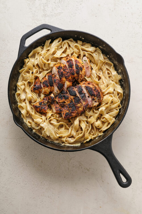 Crispy grilled chicken with creamy fettuccine alfredo in cast iron skillet.