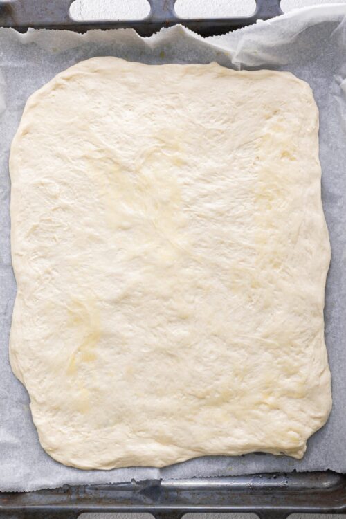 Soft, rolled-out pizza dough on baking sheet ready for baking.