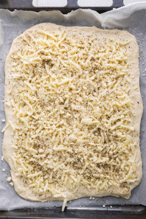 Shredded cheese and seasonings on a baking sheet before baking cheesy bread or pastry.