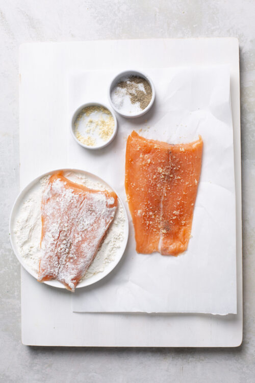 Fresh salmon fillet coated in seasonings for baking, with salt and pepper in small bowls.