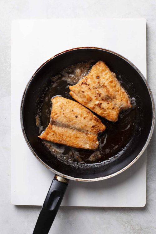 Golden seared salmon fillets cooking in a black skillet.