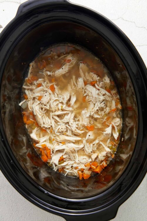 Shredded chicken and vegetables in a slow cooker soup for easy homemade meal.