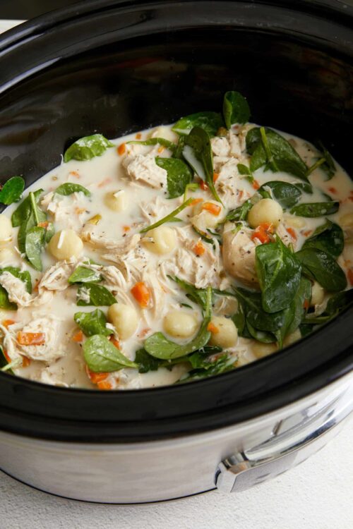 Creamy chicken and spinach stew with vegetables in a slow cooker.