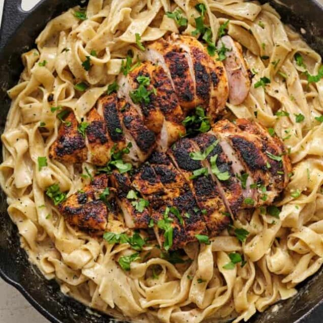 Butter chicken pasta with grilled chicken in a skillet, garnished with herbs - Baked Bree.