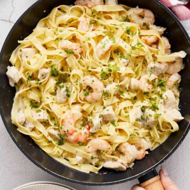 Creamy shrimp pasta in a black skillet with fresh herbs and al dente noodles, perfect for a flavorful seafood dinner, from Baked Bree.