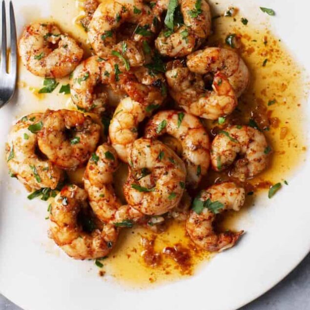 Juicy shrimp in spicy garlic butter sauce with fresh herbs on a white plate.
