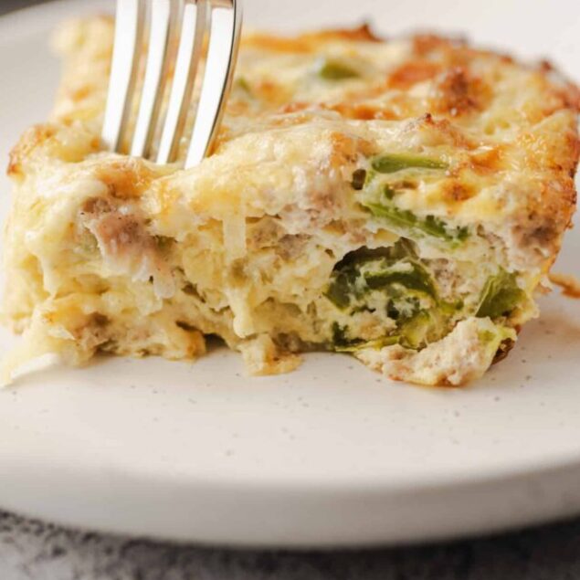 Baked cheesy casserole with vegetables on white plate.