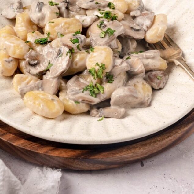 Creamy mushroom and potato gnocchi with parsley garnish on a rustic plate.