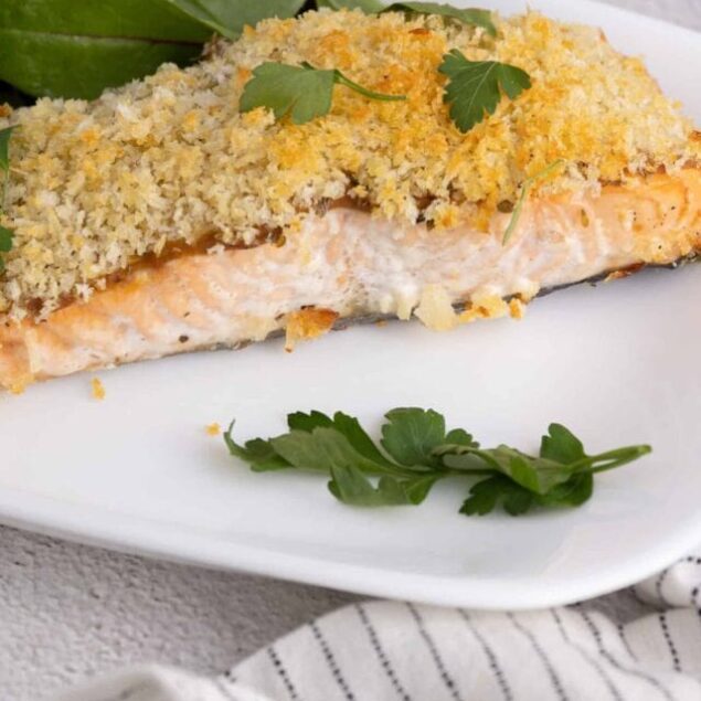 Baked salmon with crispy breadcrumb topping and fresh green salad on a white plate.