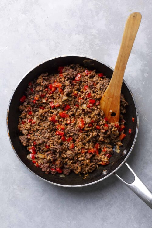 Ground beef with red peppers and onions in a skillet.