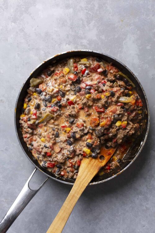 Savory ground beef and vegetable chili in a skillet with wooden spatula over gray surface.