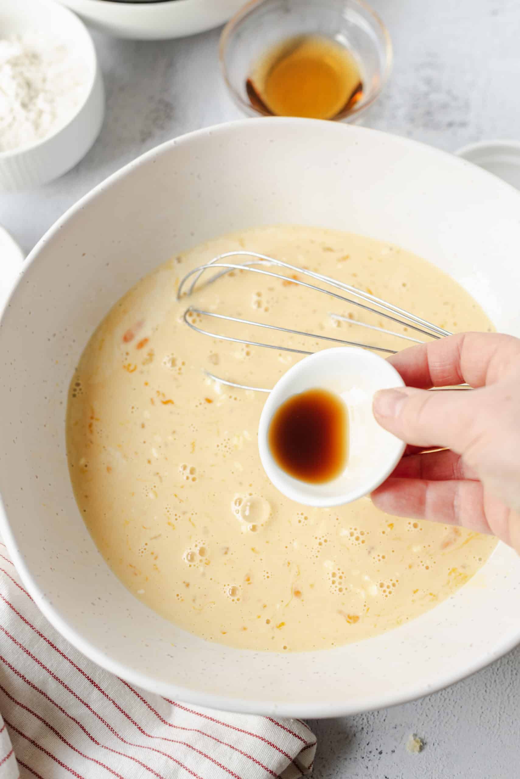Creamy batter with vanilla and eggs in a mixing bowl, with vanilla and soy sauce being added.