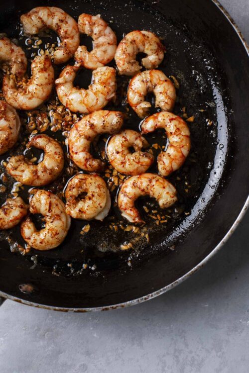 Sautéed shrimp with garlic and seasonings in a black skillet, ready for a delicious seafood dish.