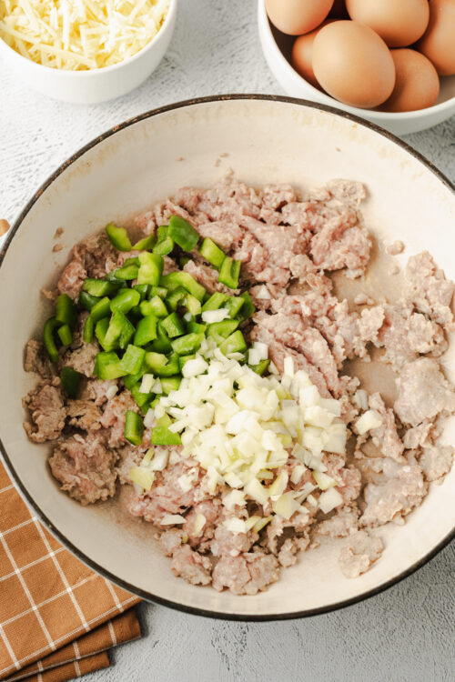 Freshly ground sausage skillet with chopped green bell peppers and onions for breakfast or Italian recipes.