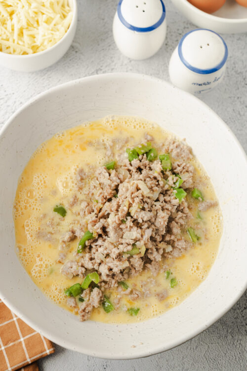 Creamy scrambled eggs with cooked sausage and green onions in a white bowl.