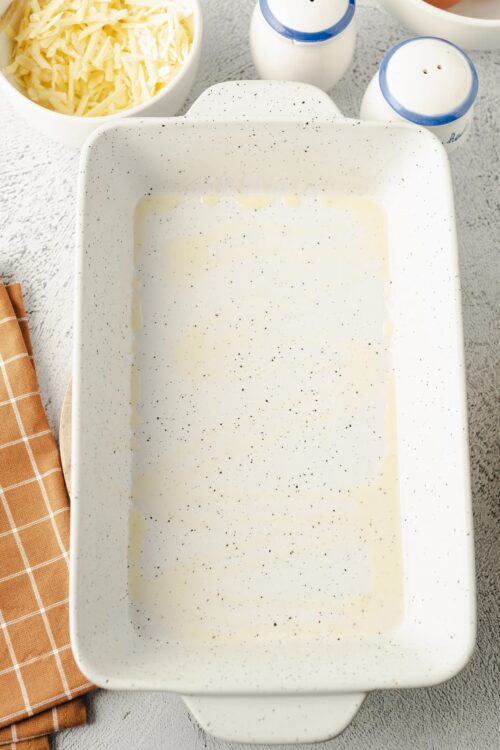 Cream-colored baking dish with leftover batter, surrounded by cheese, milk jugs, and kitchen items.