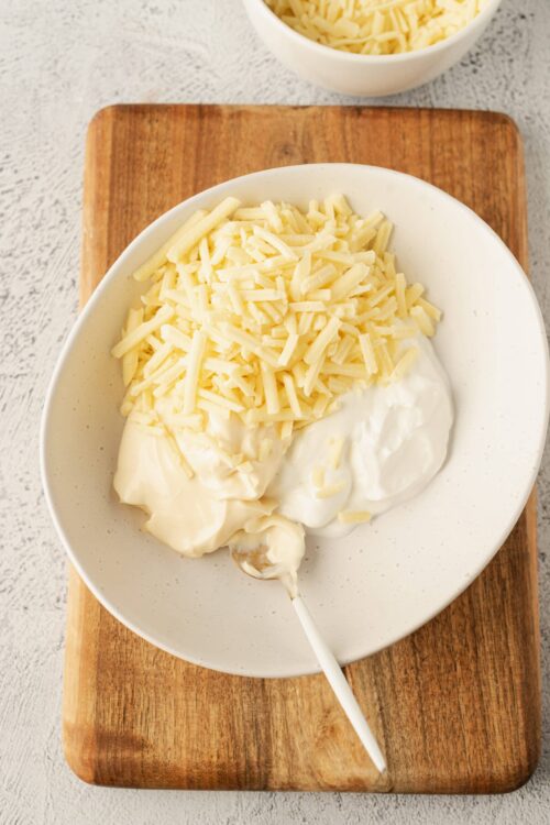 Shredded cheese and cream cheese in a white bowl, ready for baking or cooking.