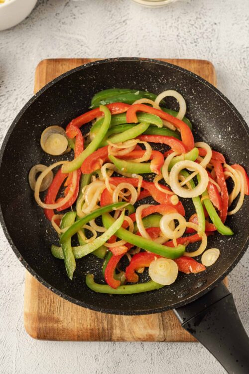 Colorful sliced bell peppers cooking in a black skillet on a wooden cutting board.