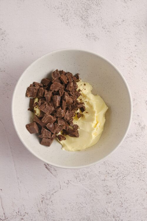 Rich chocolate chunks and creamy butter in a white bowl, ready for baking or dessert preparation.