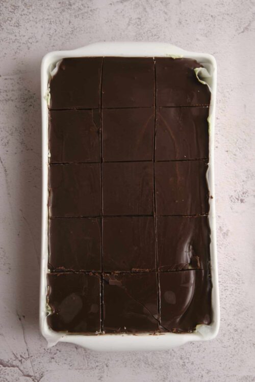 Rich chocolate dessert topped with glossy ganache in a white rectangular dish.