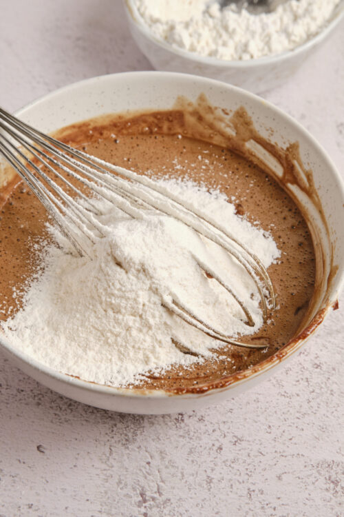 Flour being added to chocolate cake batter in a mixing bowl.