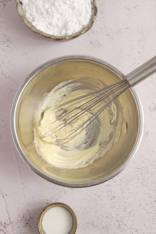 Cream cheese and butter being whipped in a stainless steel mixing bowl for baking recipes.