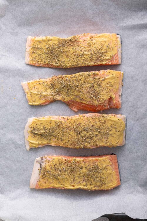 Seasoned salmon fillets with herbs on baking sheet prepped for cooking.