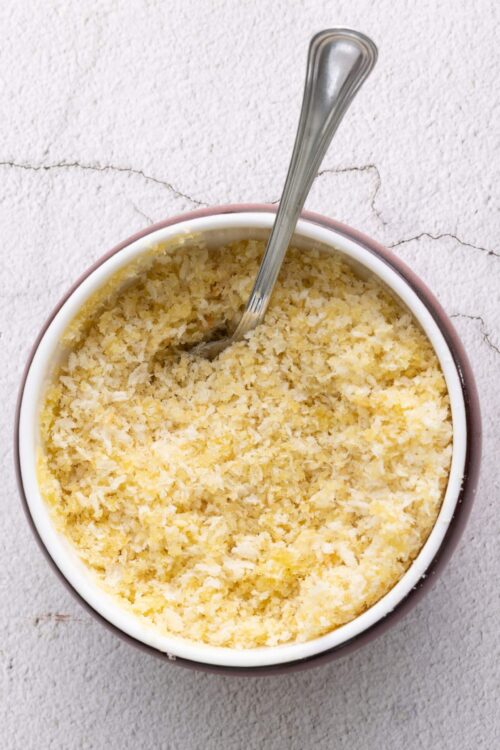 Buttery homemade breadcrumb topping in a white bowl with a silver spoon, perfect for baked dishes.