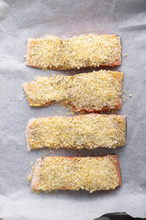 Golden breaded salmon fillets on parchment paper ready for baking.