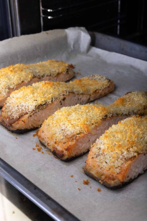 Baked salmon fillets with breadcrumb topping on baking sheet.