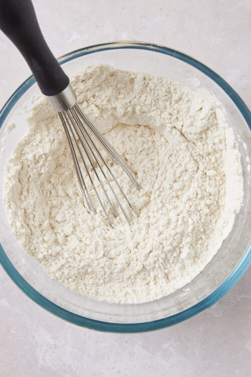 Finely ground flour in glass mixing bowl with whisk, baking ingredients for homemade baked goods.