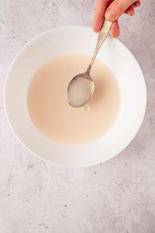 Creamy vanilla bean extract in a white bowl with a silver spoon.