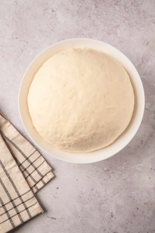 Fresh pizza dough proofing in a white bowl ready for baking.