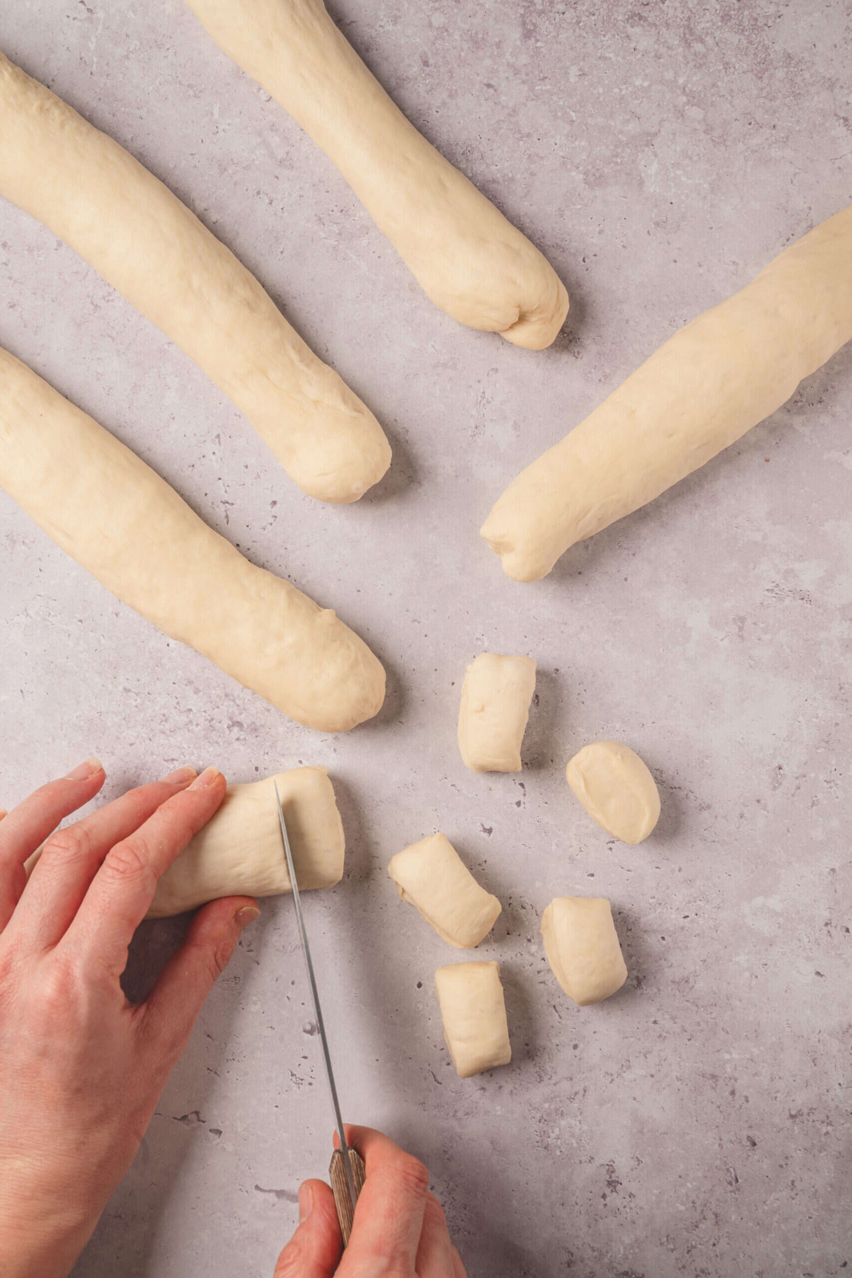 Buttered bread dough being sliced into small pieces for baking.