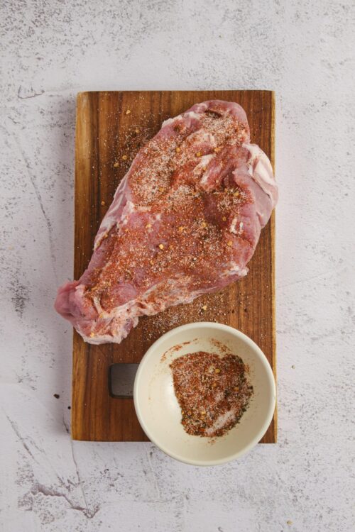 Seasoned raw pork tenderloin with spice rub on wooden cutting board, ready for cooking.