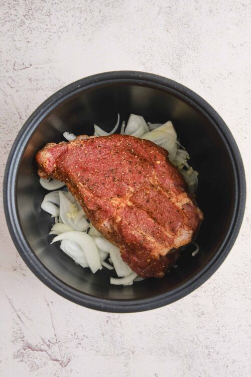 Juicy seasoned pork chop in a slow cooker on onion slices for easy dinner.