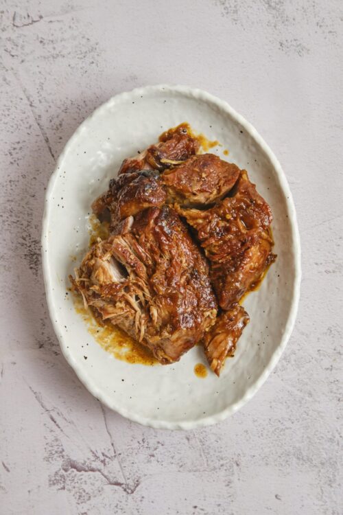 Tender pulled pork in smoky barbecue sauce on a white ceramic plate.