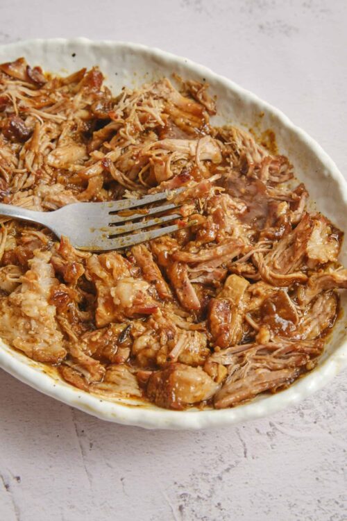 Fall-apart shredded chicken in flavorful barbecue sauce, served in a rustic white dish. Perfect for easy weeknight dinners or meal prep.