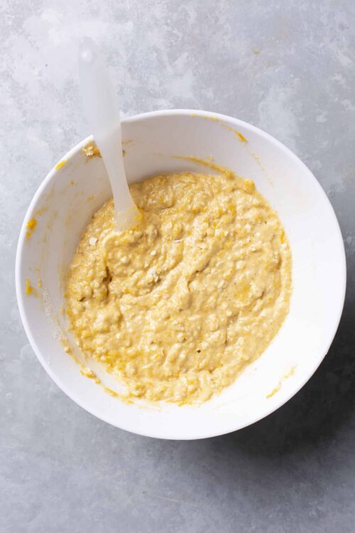 Creamy banana bread batter in a white bowl with a white spatula, ready for baking.