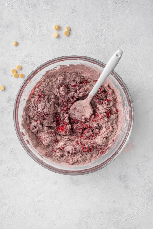 Sweet berry muffin batter in glass bowl with spoon on white countertop.