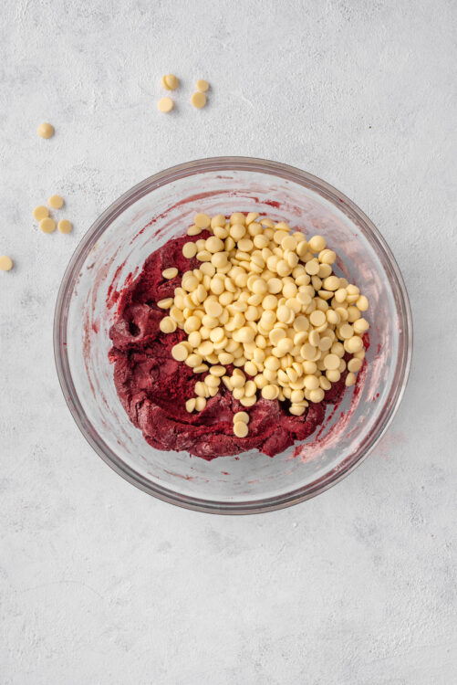 Creamy white chocolate chips over vibrant red cookie dough in a glass bowl.